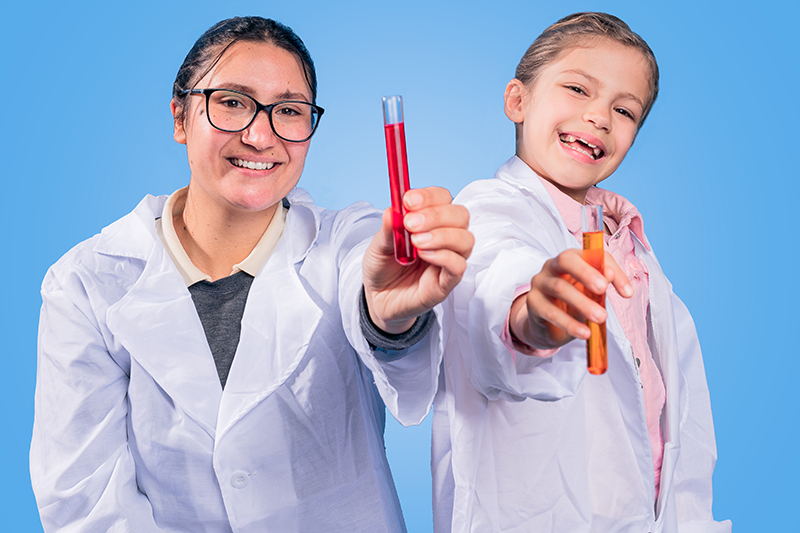 A woman and a girl in white lab coats hold test tubes of coloured liquid.
