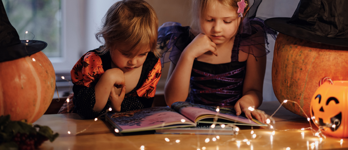 photograph of two children in halloween costumes reading a spooky story from a book