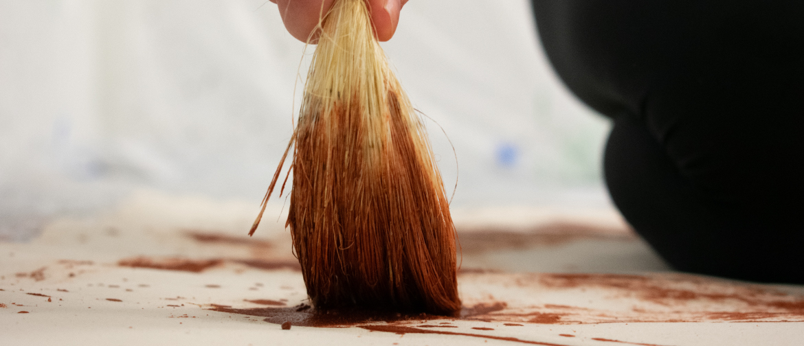 Photograph of an artist's hand painting with a piece of rope