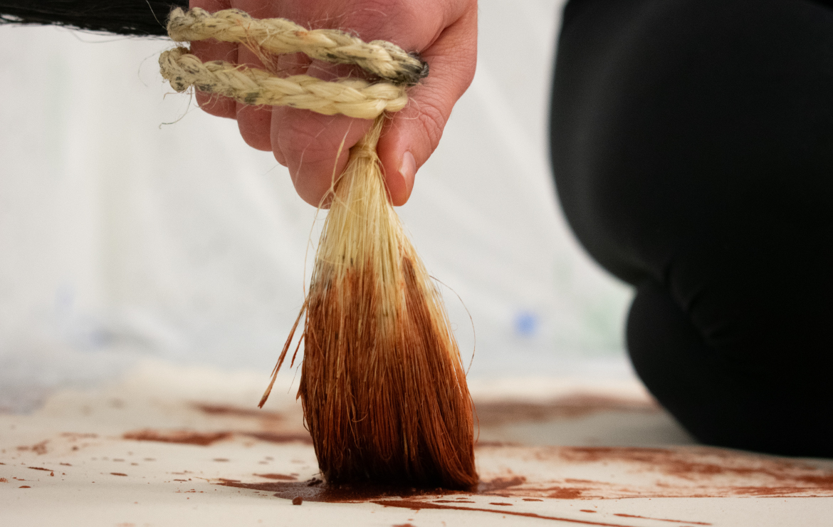 Photograph of an artist's hand painting with a piece of rope