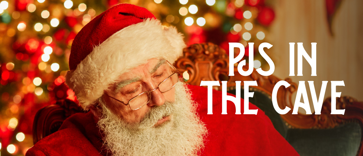 photograph of santa sitting in front of a christmas tree reading a book